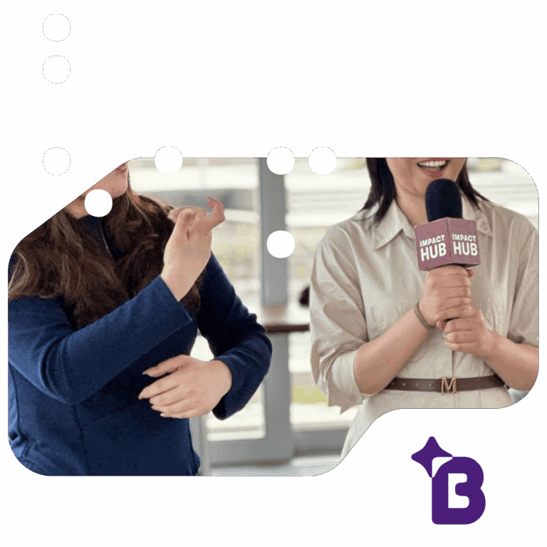 A woman on the right holds a microphone labeled “Impact Hub” while smiling, as another woman beside her uses sign language.